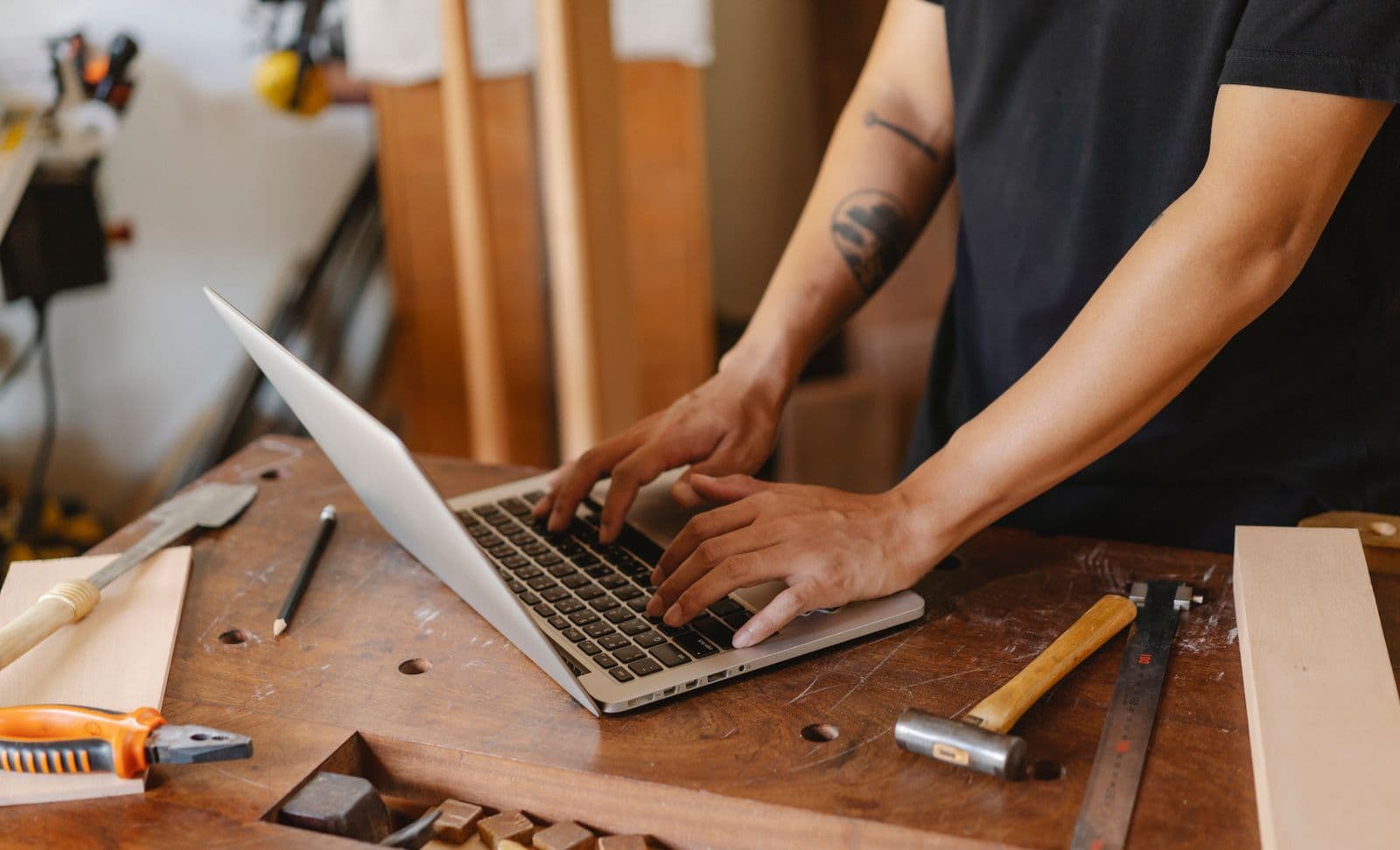 A tradesman typing on a laptop at a workbench covered in tools