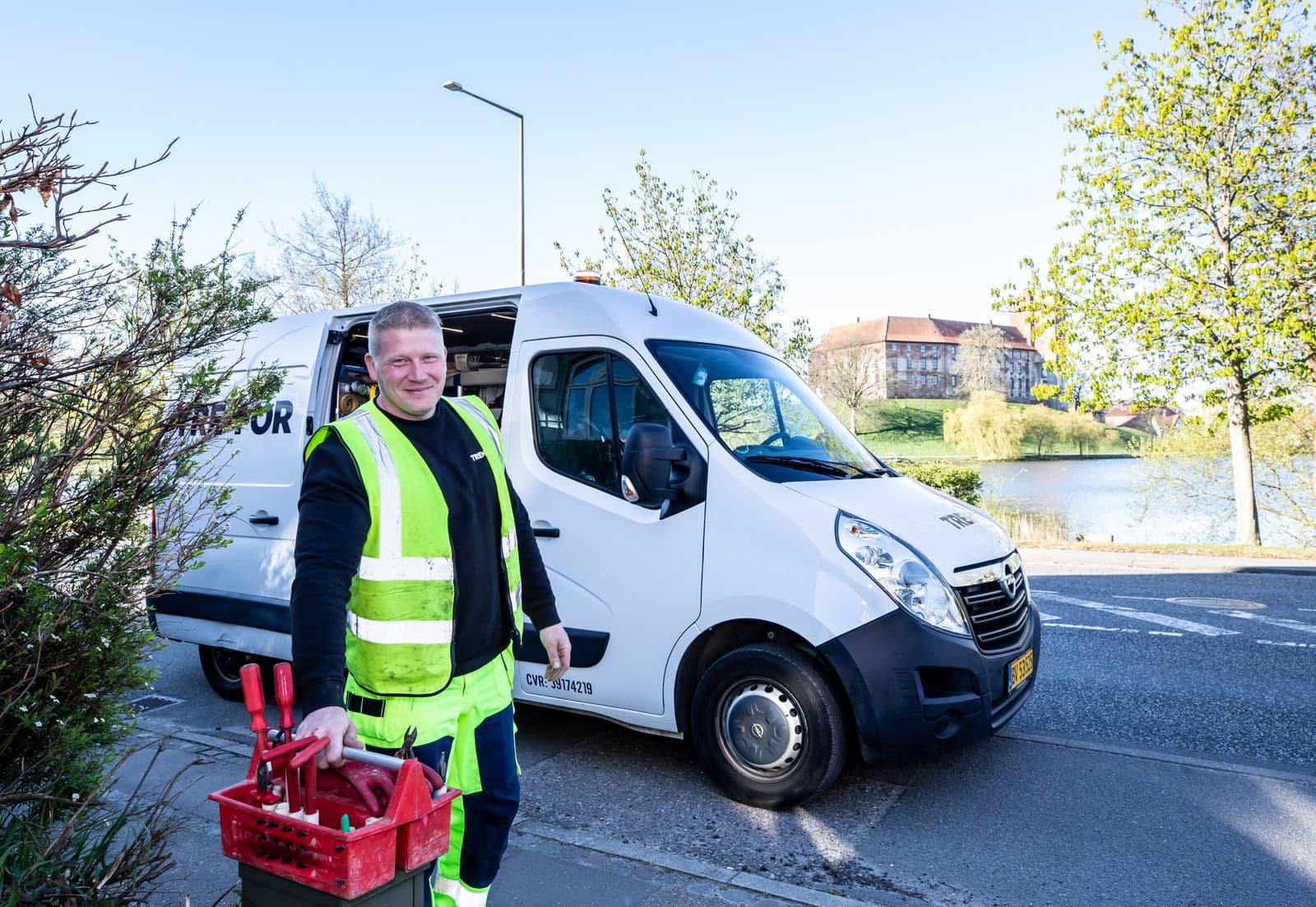 A smiling tradesman in a high-vis vest standing beside his white work van