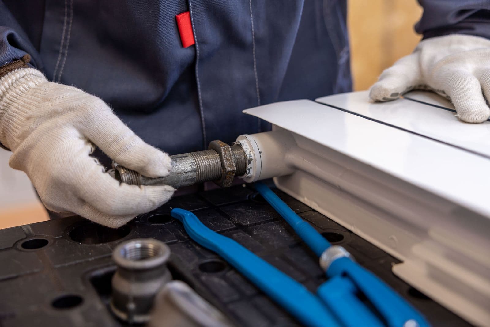 A plumber in work gloves fitting a threaded pipe to a radiator