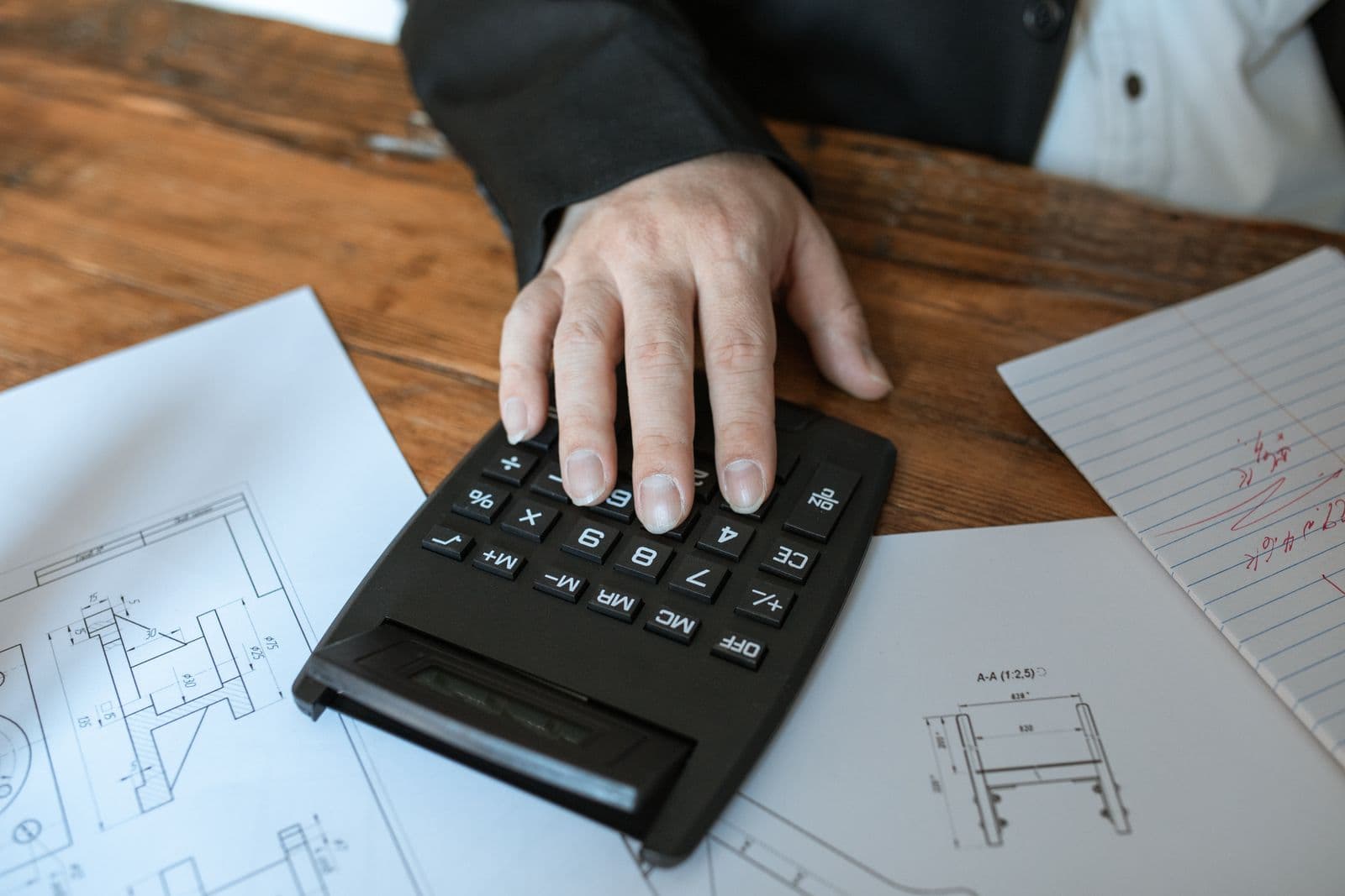 A hand working figures out on a desk calculator beside paperwork